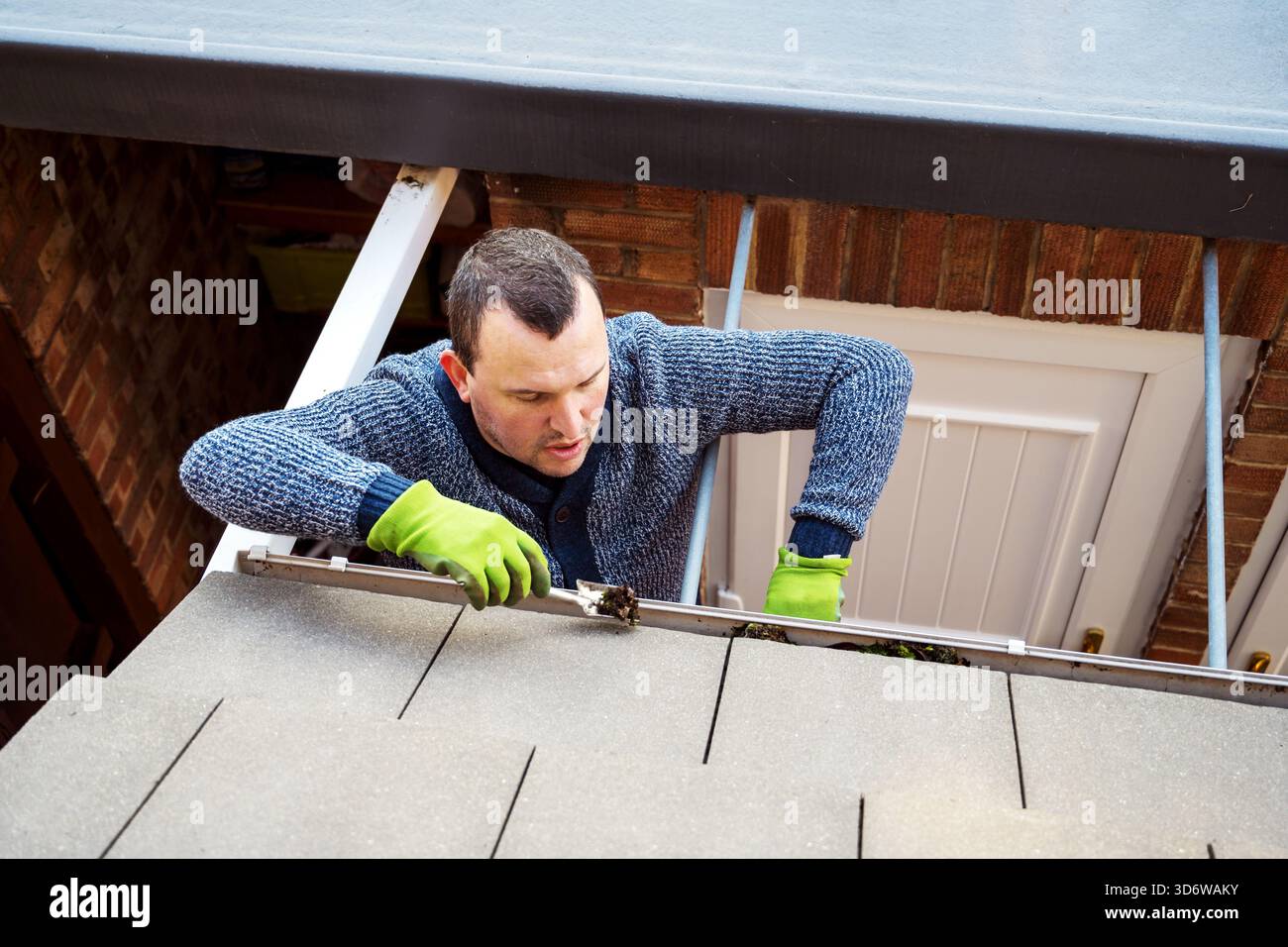 Man on a ladder cleaning fallen autumn leaves and moss from house roof ...