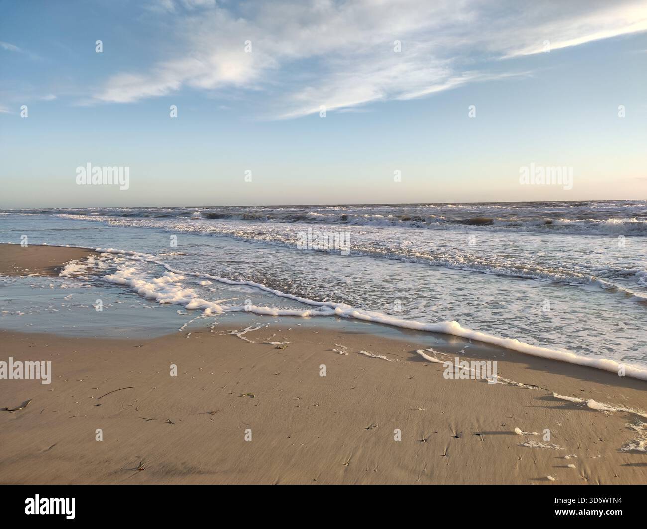 Calm sandy beach with waves at sunset,blue sky and gold sand - Smartphone Captured Stock Image
