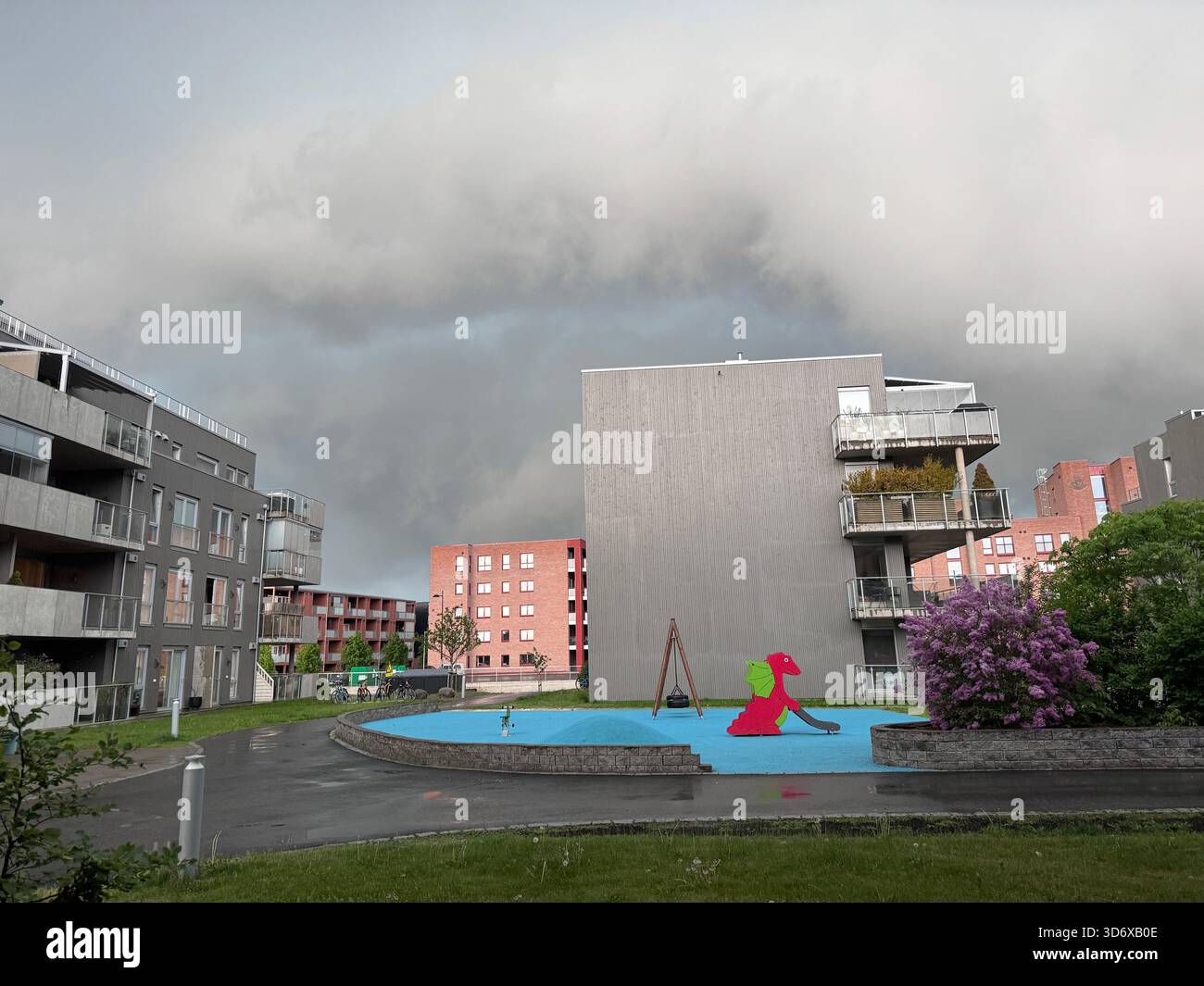 Dark dramatic clouds loom above modern apartment buildings and a small colorful playground after rainfall. - Smartphone Captured Stock Image