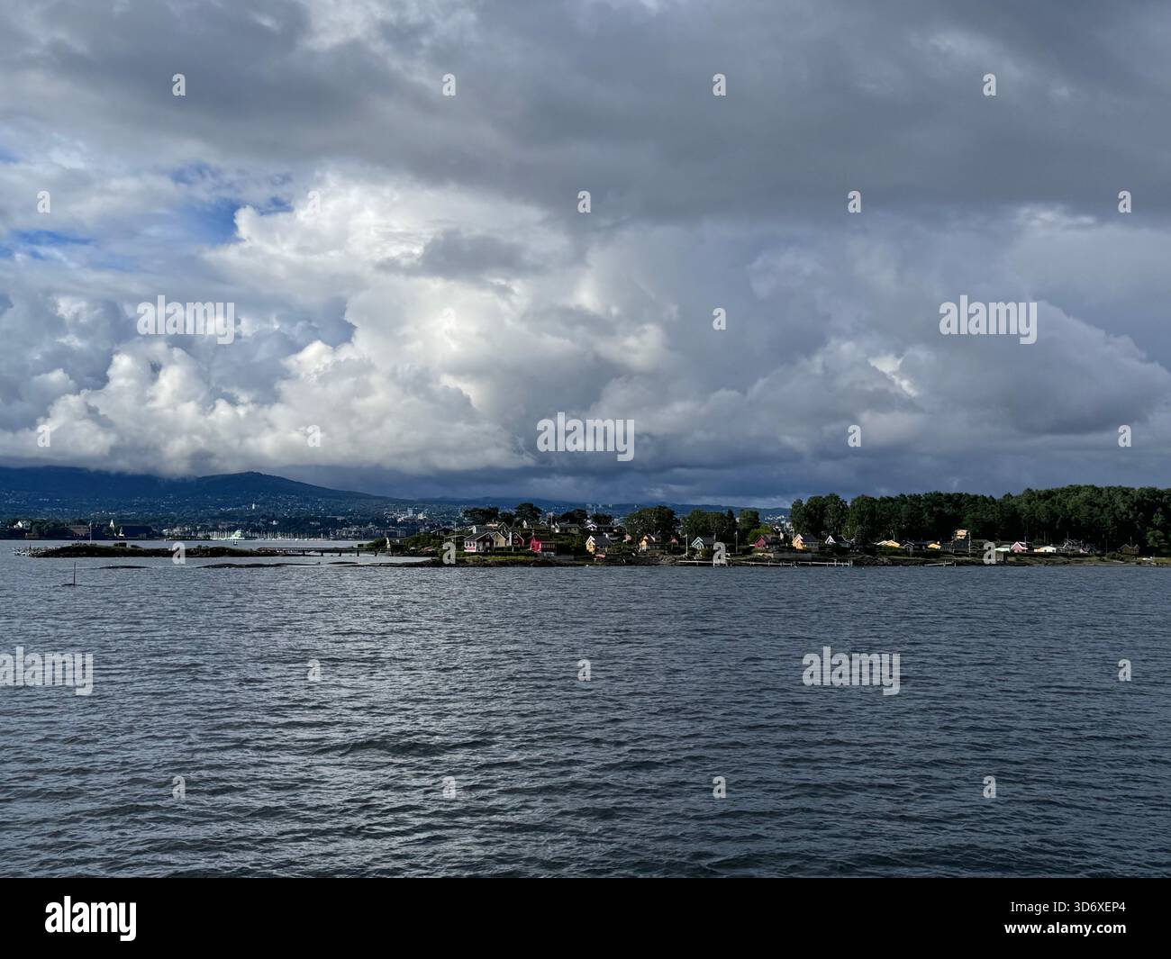 A small coastal village sits along the water, framed by rolling hills and dramatic layered clouds. - Smartphone Captured Stock Image