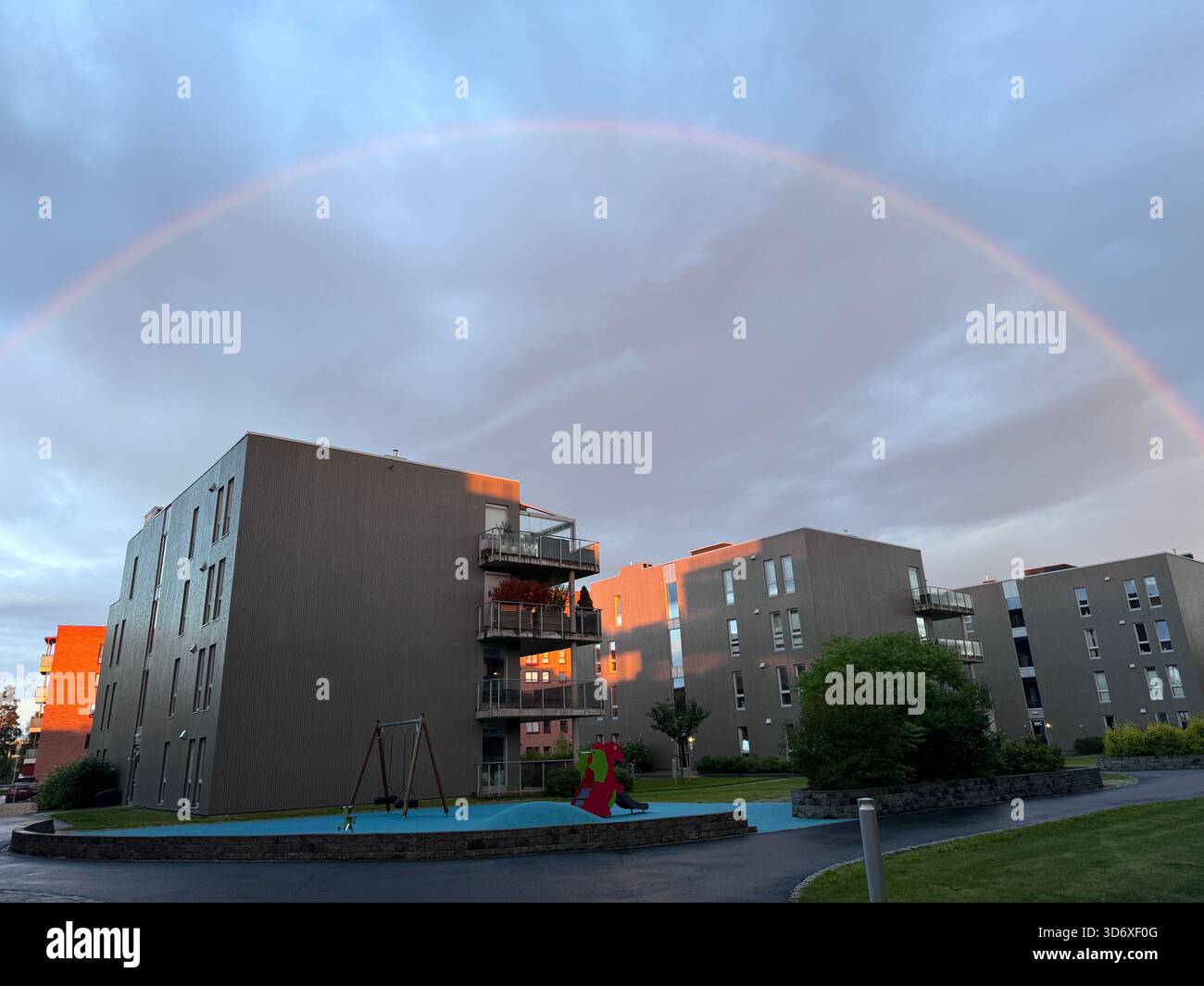 A soft rainbow arches over modern apartment buildings, glowing in warm evening light. - Smartphone Captured Stock Image