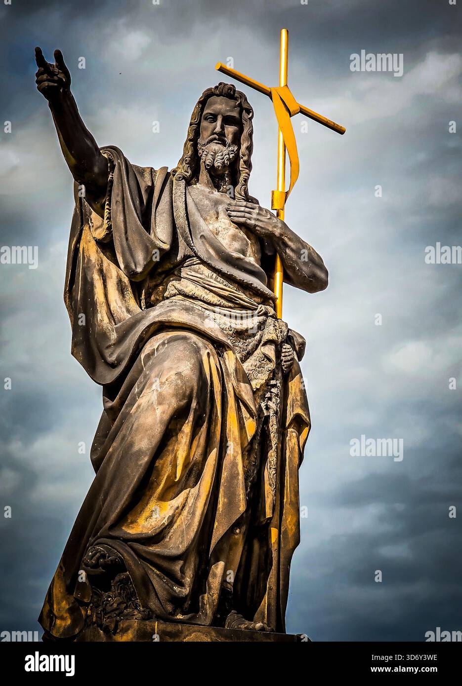 Dramatic statue of a saint holding a golden cross on Charles Bridge ...