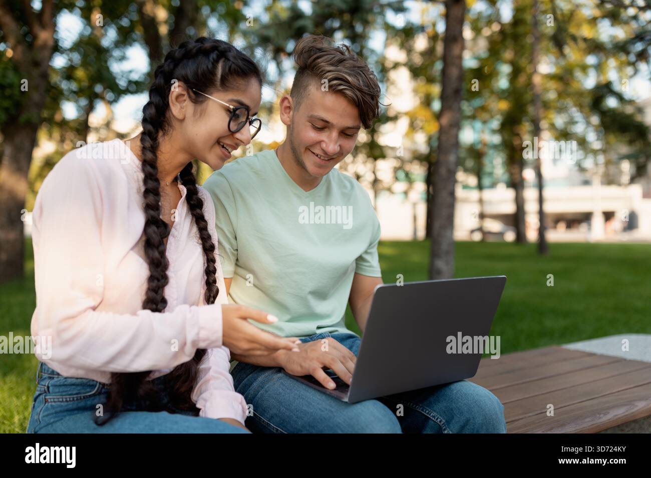 Teenagers Collaborating on a Laptop in a Sunny Park While Enjoying Their Time Outdoors Stock Photo