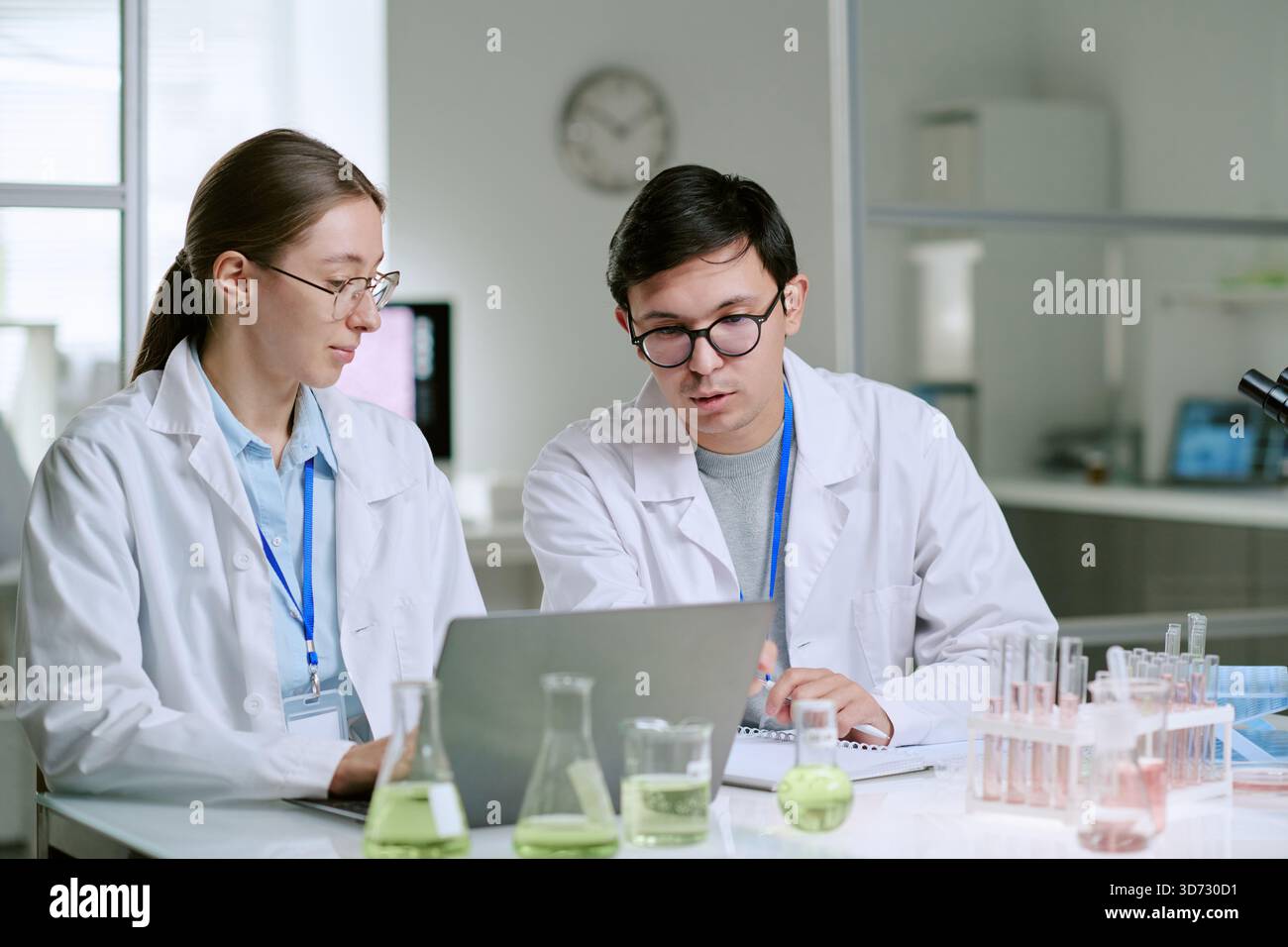 Young Caucasian Man and Woman Analyzing Medical Data on Laptop in Laboratory Stock Photo