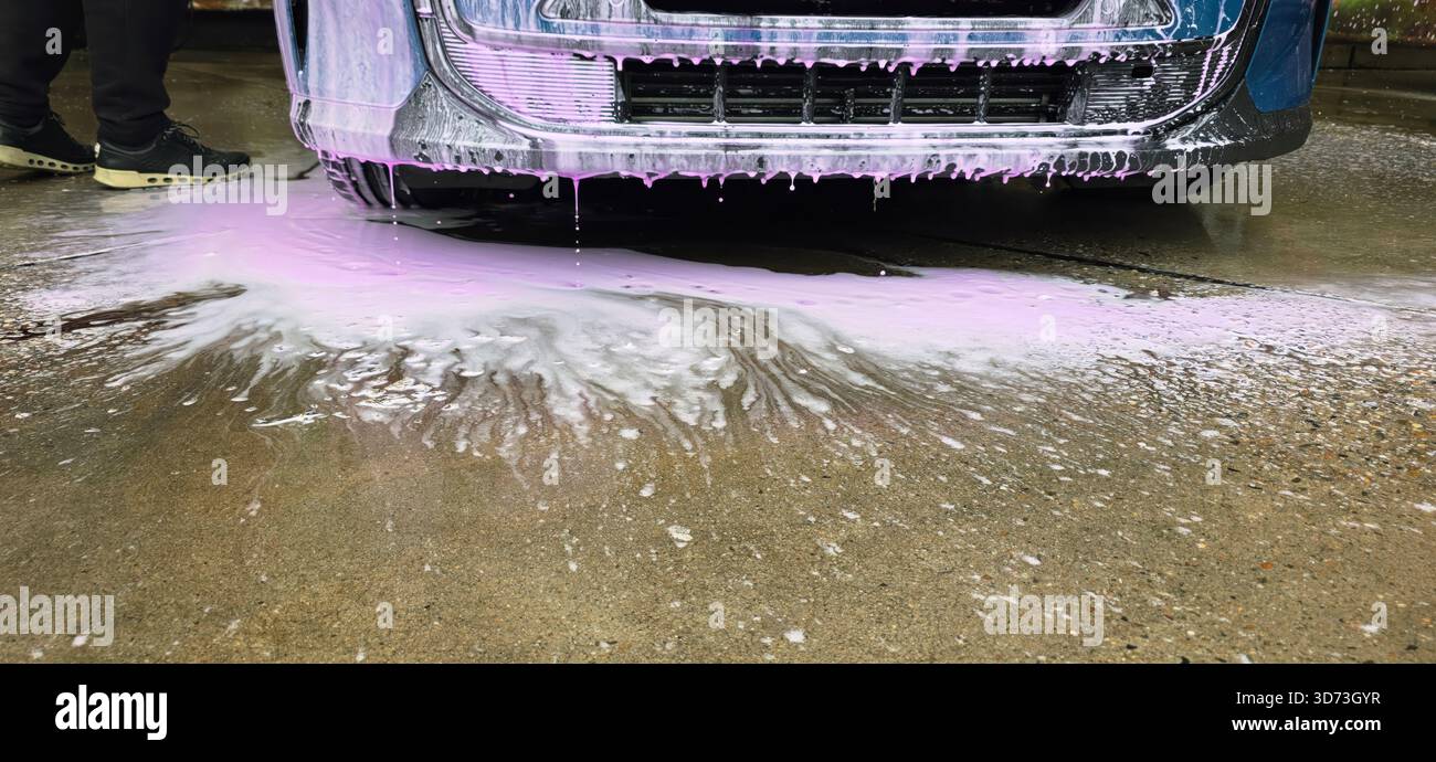 Berlin, Germany - May 18, 2025: Car is being washed with pink foam soap on driveway, creating water splashes around. - Smartphone Captured Stock Image