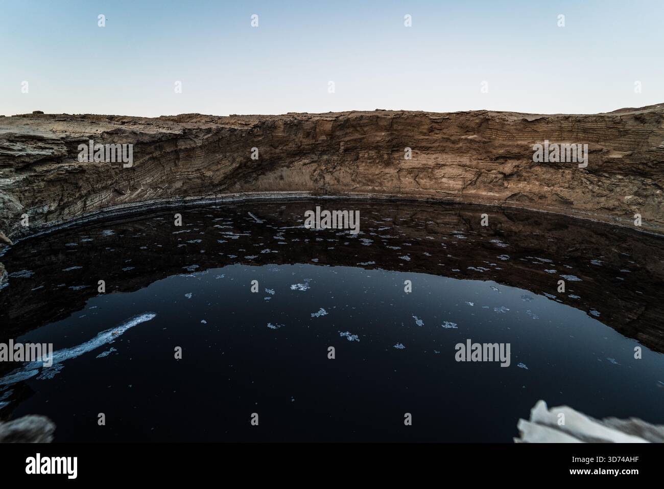 Unique Dead Sea sinkhole with dark black water surrounded by the salt crust and mineral formations, contrasting tones on the exposed shoreline. Stock Photo