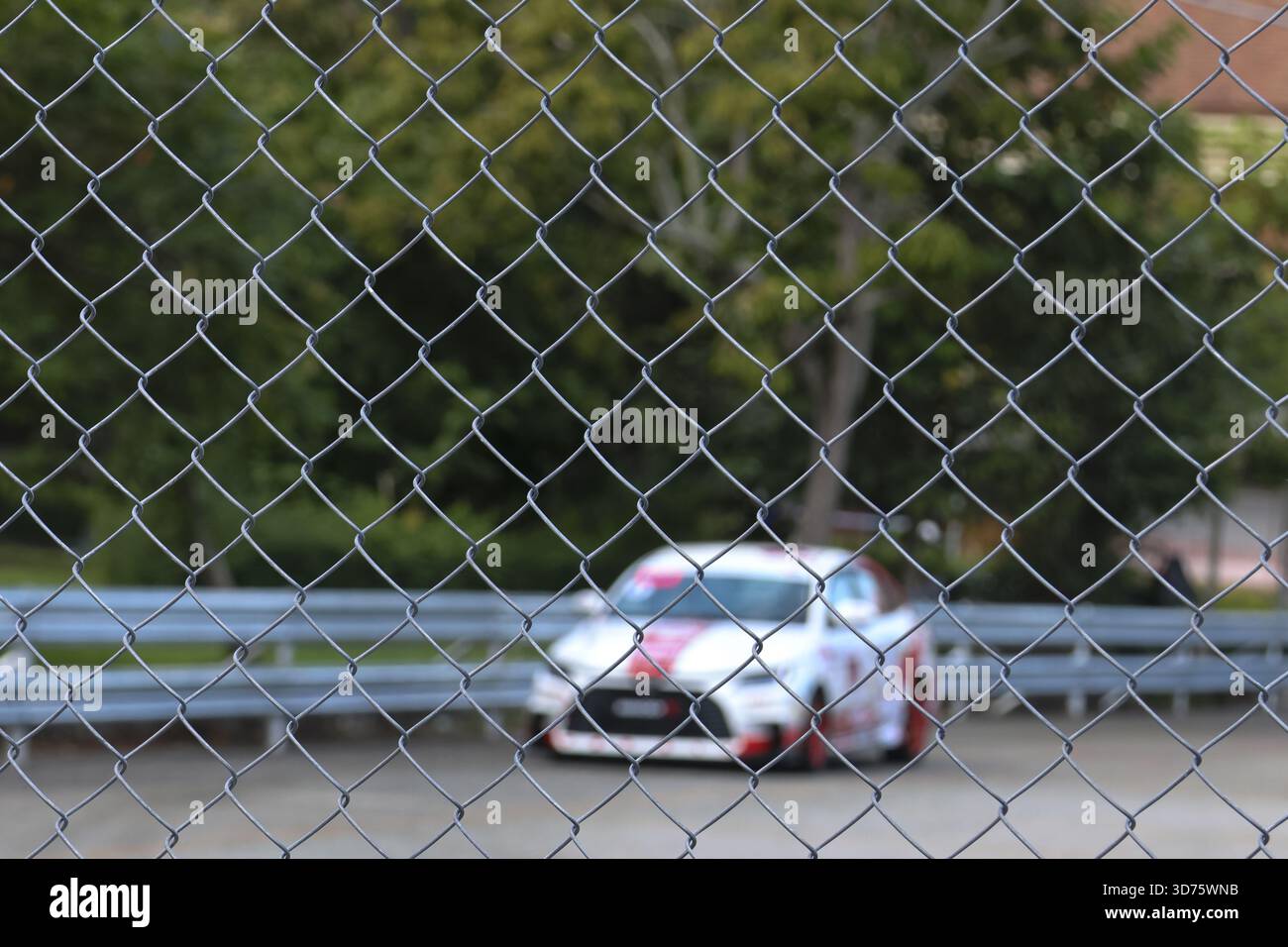 Blurred view of white sports car on race track behind chain link fence.  background gives feeling of separation from fast speed and outdoor  competition Stock Photo - Alamy