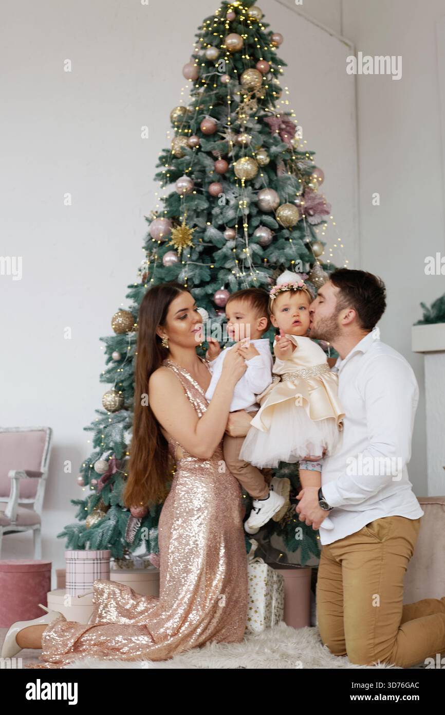 parents formal dress A family poses together in an elegant setting. The wear outfits and hold their children, smiling joyfully in front of a decorated Chris Stock Photo mother parents wedding dress