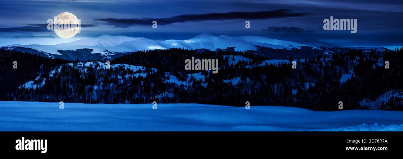 panorama of mountain ridge in winter at night. magnificent alpine landscape with snowy peaks with cloudy sky in full moon light. backdrop for fiction Stock Photo