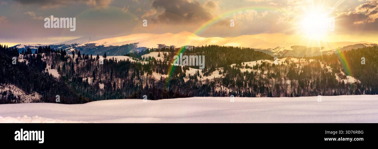 panorama of mountain ridge in winter at sunset. magnificent alpine landscape with snowy peaks with cloudy sky in evening light. storytelling cinematic Stock Photo