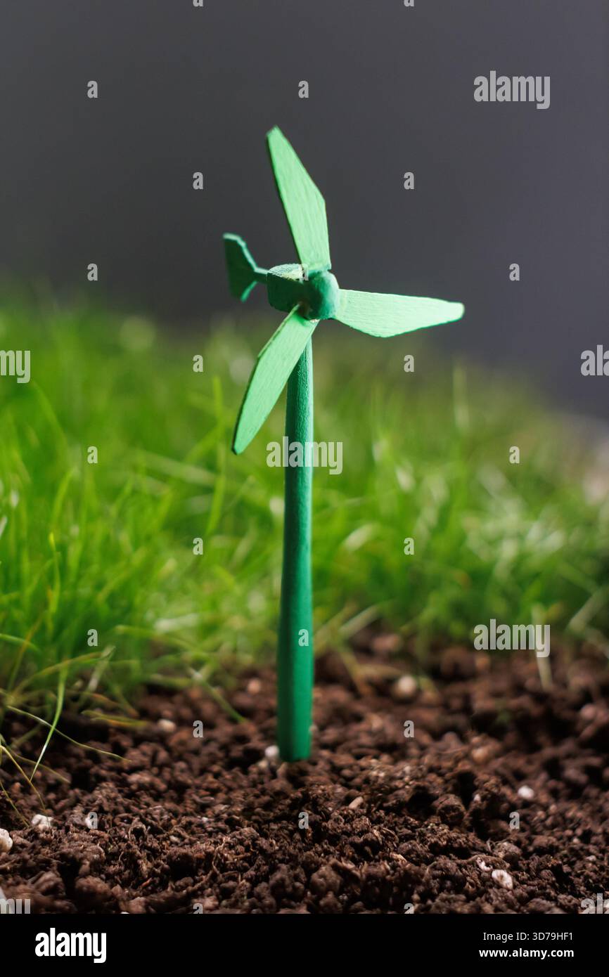 Small green wind turbine model placed in soil with green grass background Stock Photo