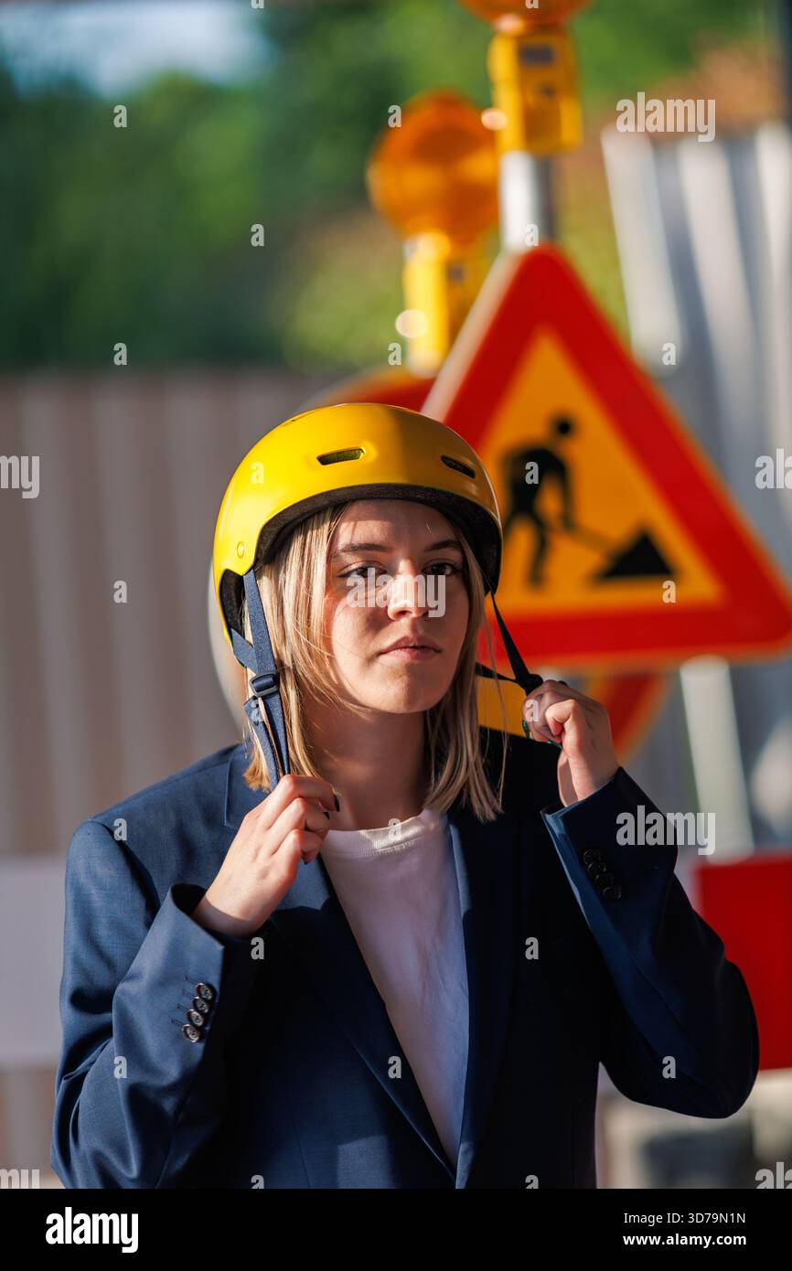 Young woman putting on a yellow helmet in front of a construction site Stock Photo