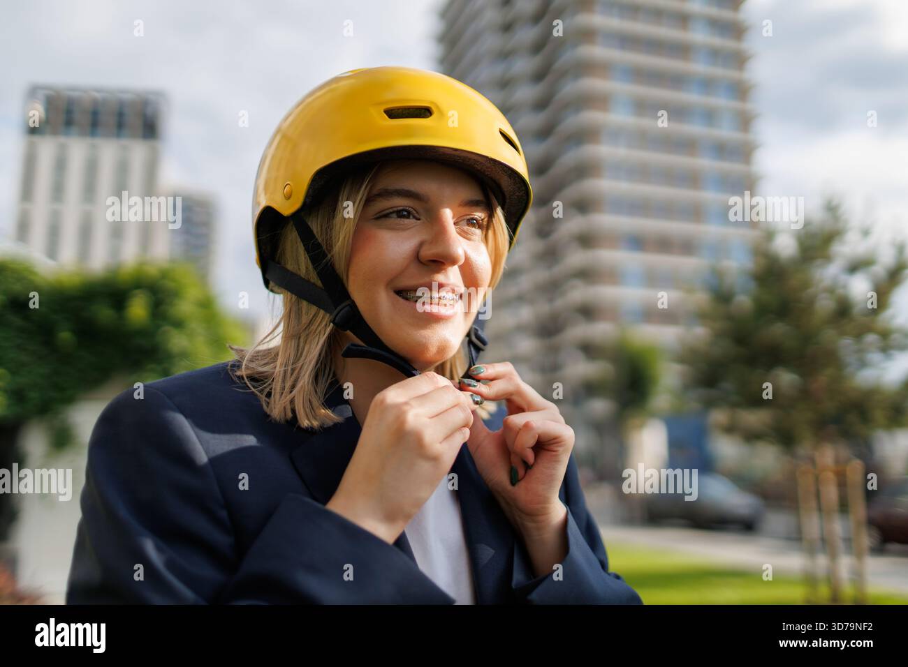 Young woman with teeth braces putting on a yellow helmet while preparing for cycling in the city Stock Photo