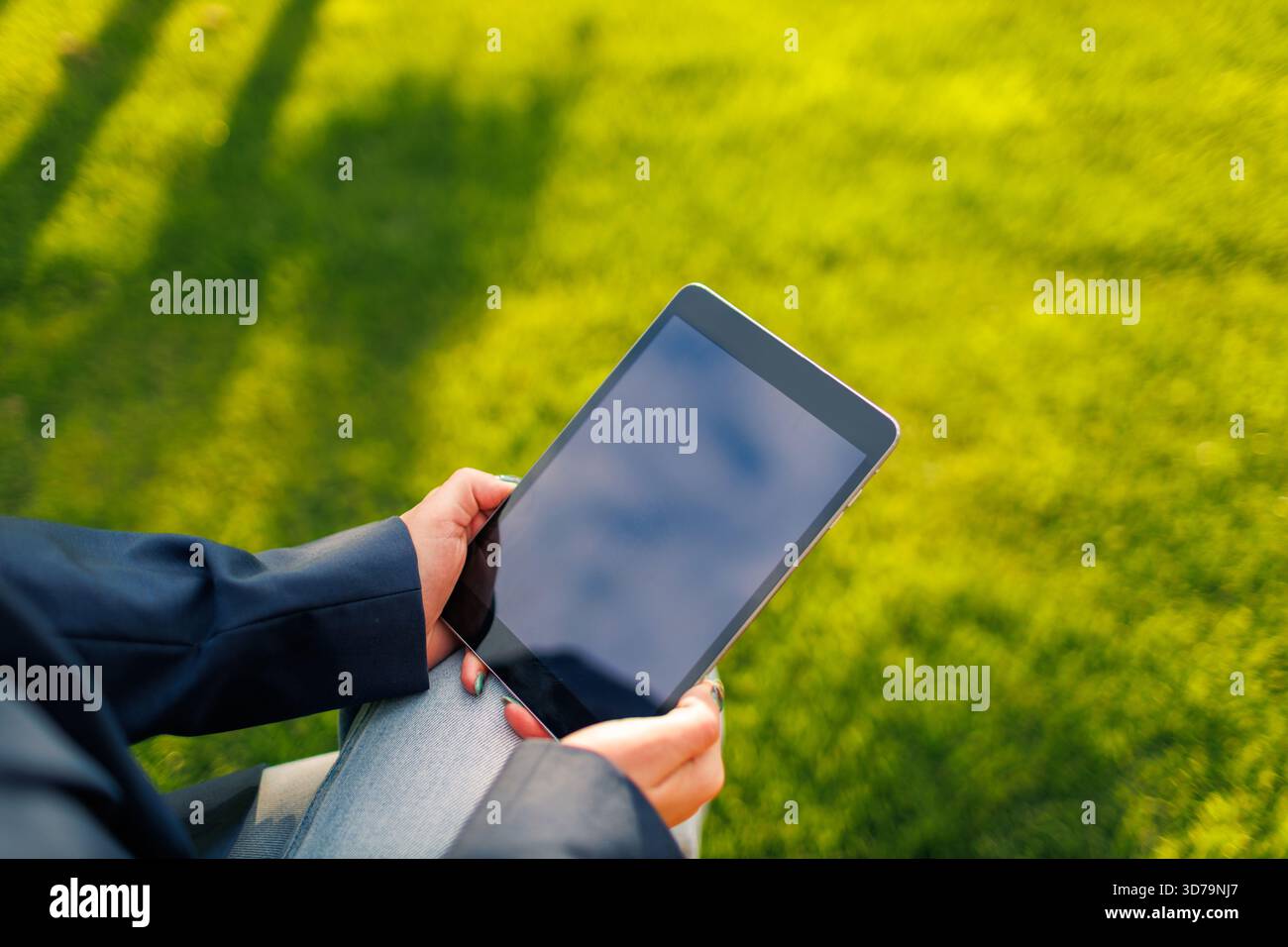 closeup of woman holding a tablet while sitting on green grass Stock Photo