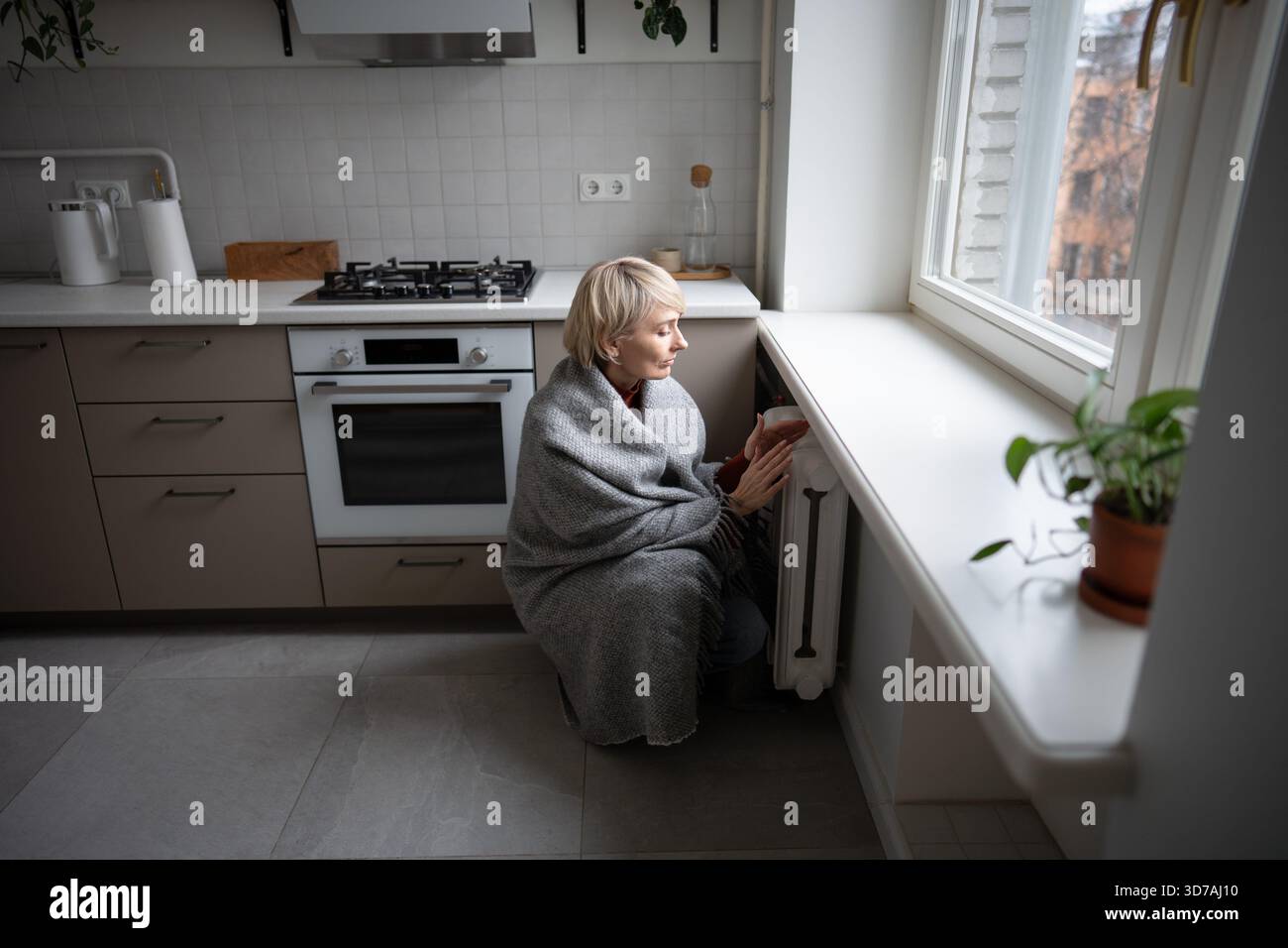 Woman warming hands on battery at home during winter. inadequate heating highlight, coldness indoor. Stock Photo