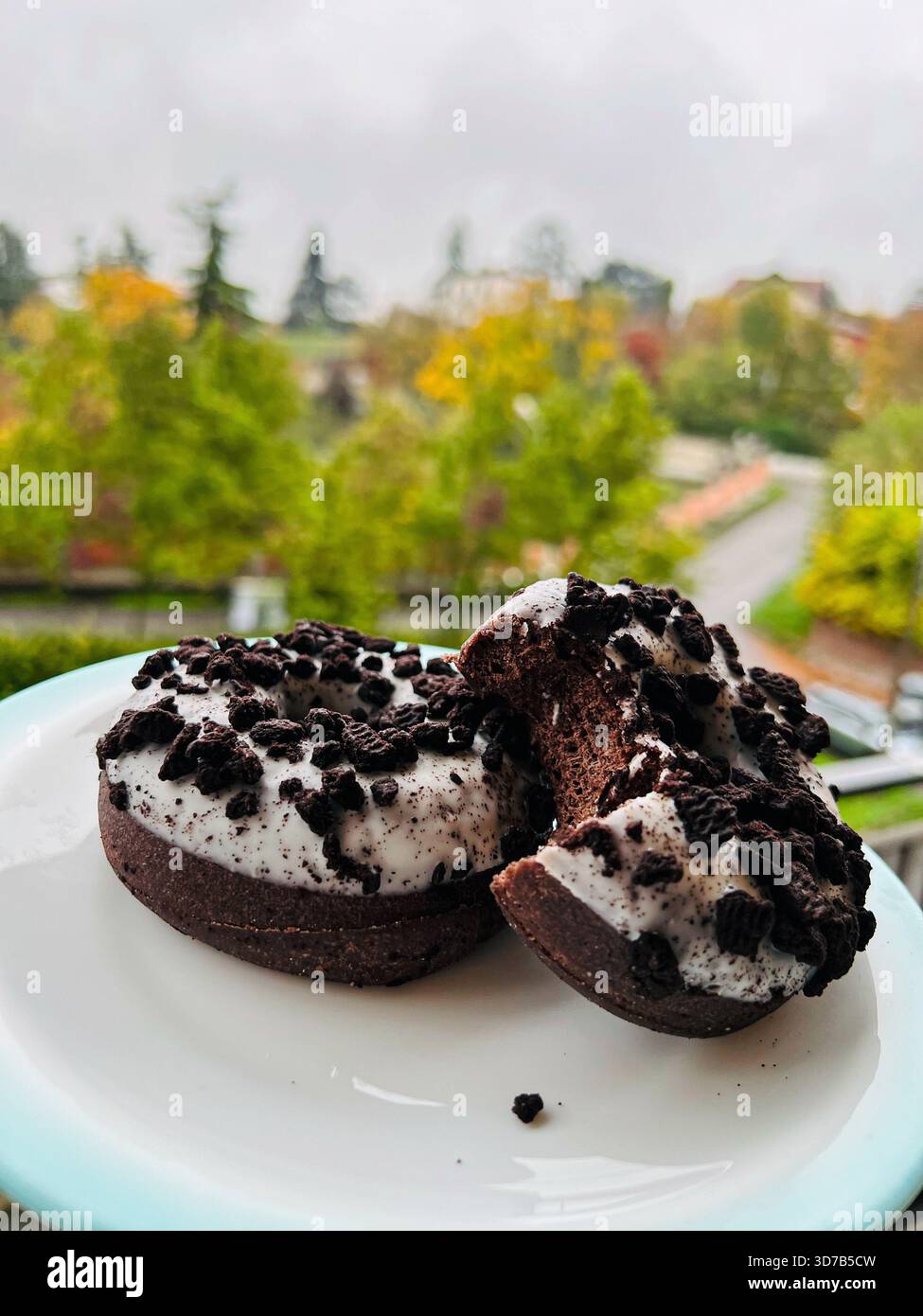 Tempting chocolate doughnuts featuring a rich Cookies and Cream topping. Two glazed pastries are set against a soft-focus - Smartphone Captured Stock Image