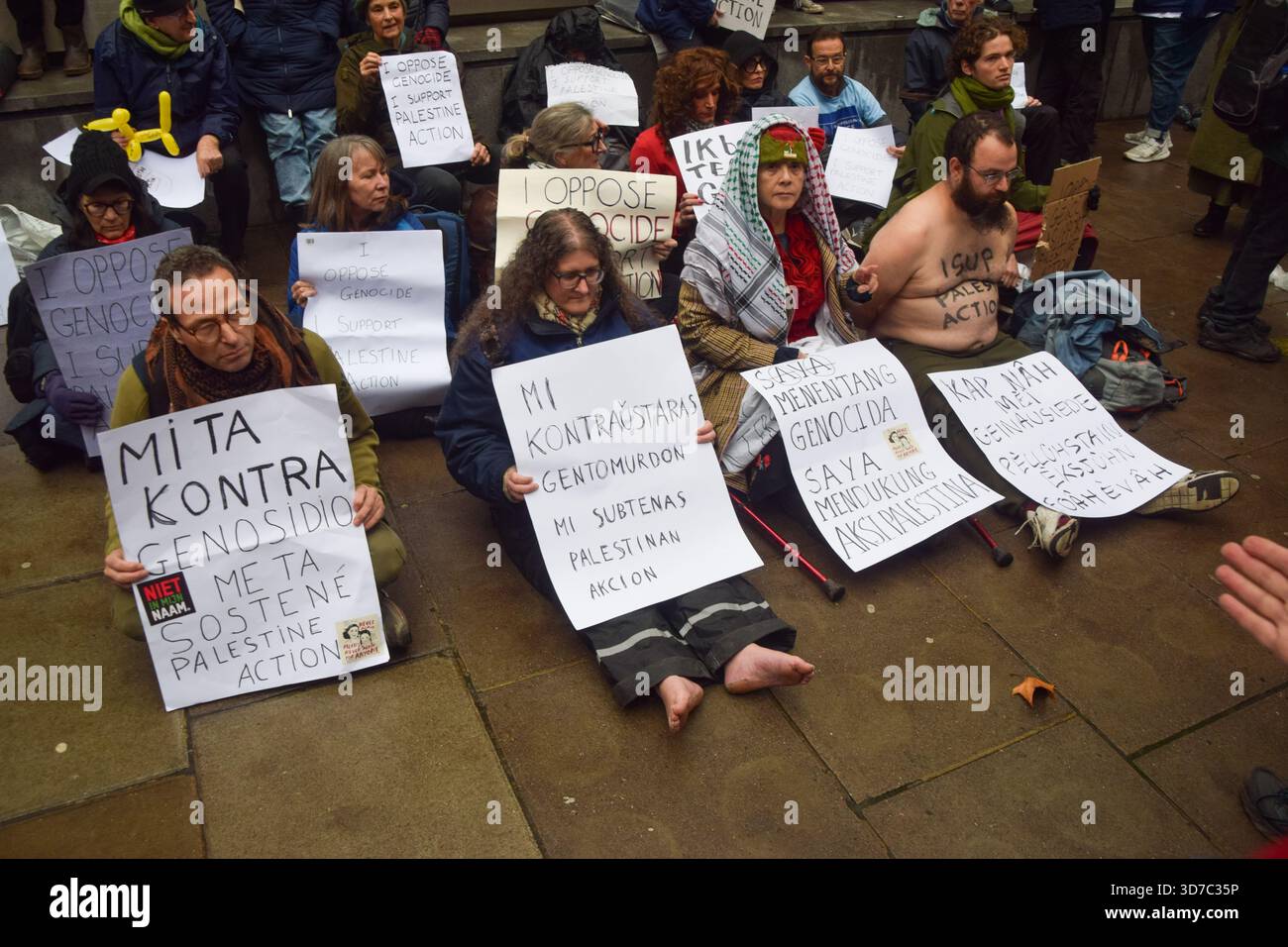 Protesters sit with a placard stating 'I oppose genocide, I support ...