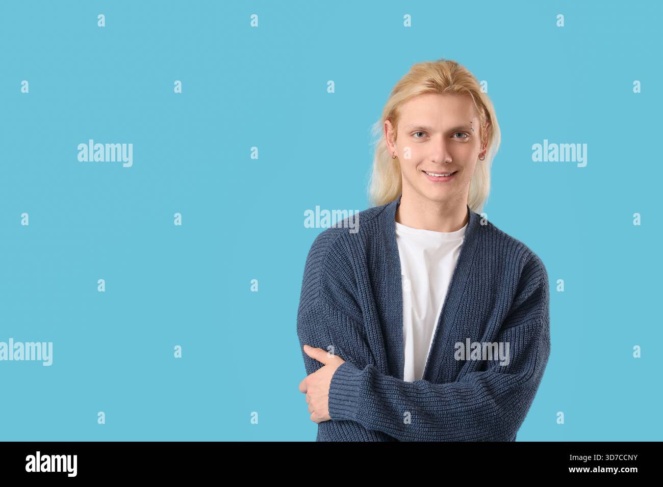 Young blonde man in cardigan on blue background Stock Photo