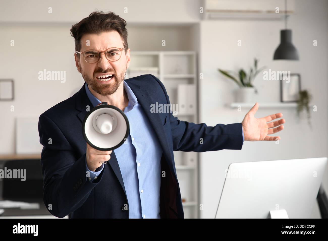 Angry businessman shouting into megaphone in office Stock Photo