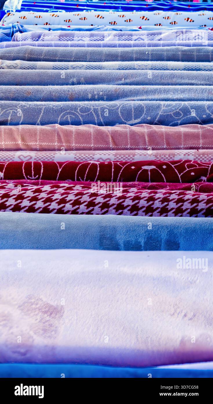 Rolled textiles arranged in layers showing various patterns like houndstooth, cartoon bears, and checks, offering many choices Stock Photo