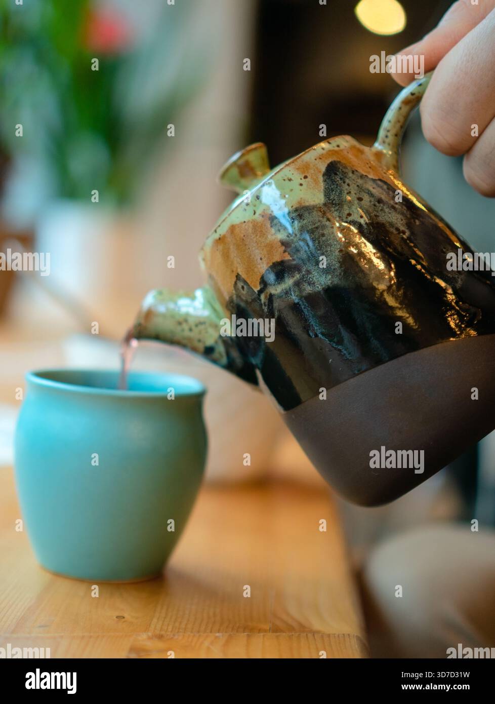 Fresh hot tea is poured from teapot into authentic cup in cozy cafe interior. Relaxing atmosphere, traditional tea ceremony, aromatic beverage, and casual restaurant setting. Stock Photo
