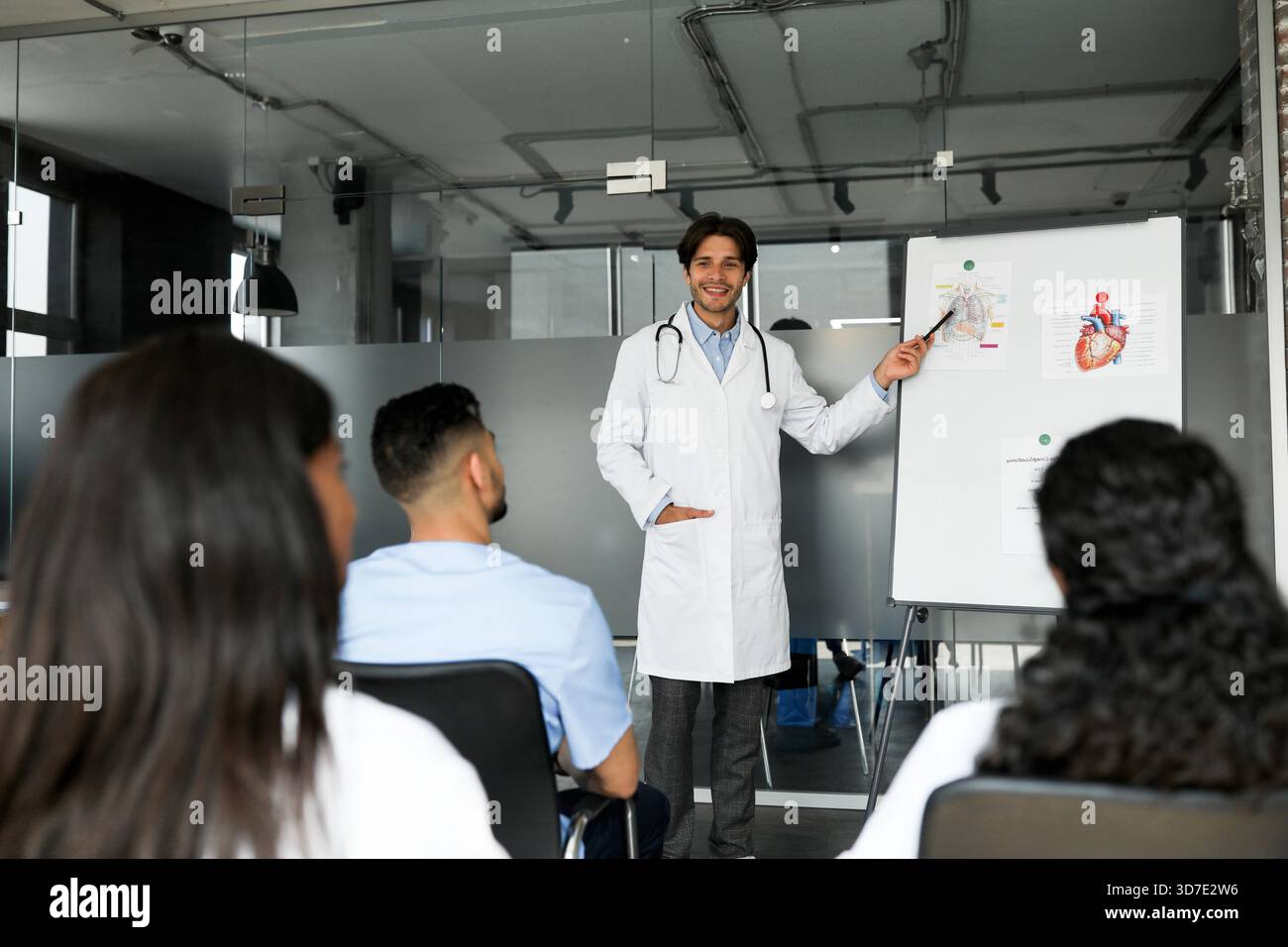 Cheerful man doctor standing next to presentation board, having speech Stock Photo