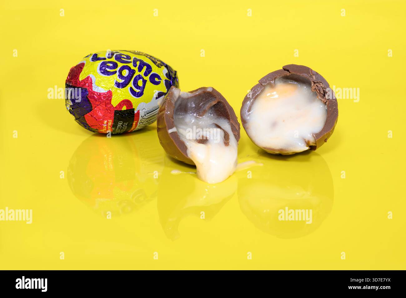 Cadbury Creme eggs on yellow background with one cut in half showing the gooey fondant oozing out Stock Photo