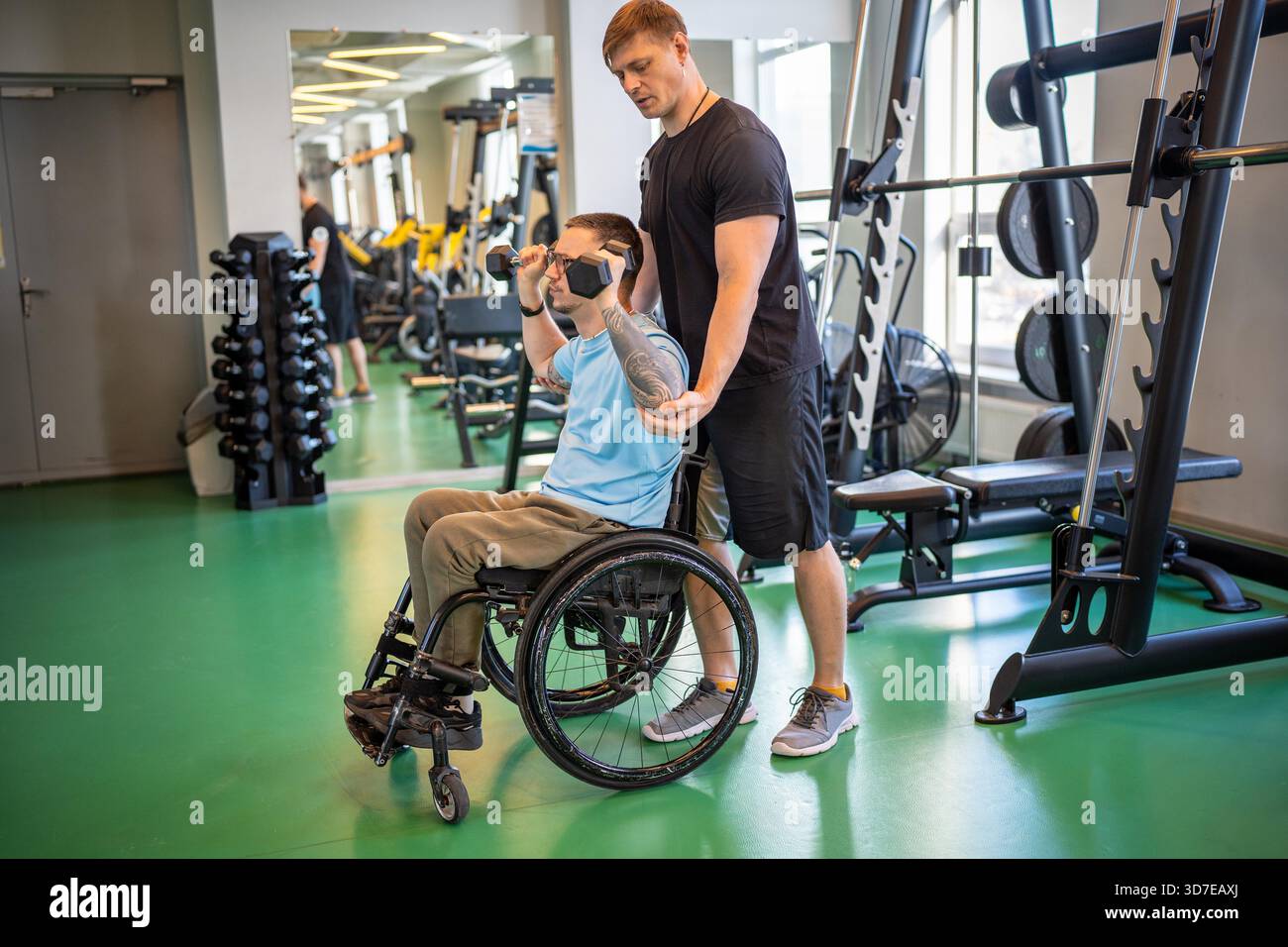 Trainer assists young man in wheelchair on personal session at gym ...