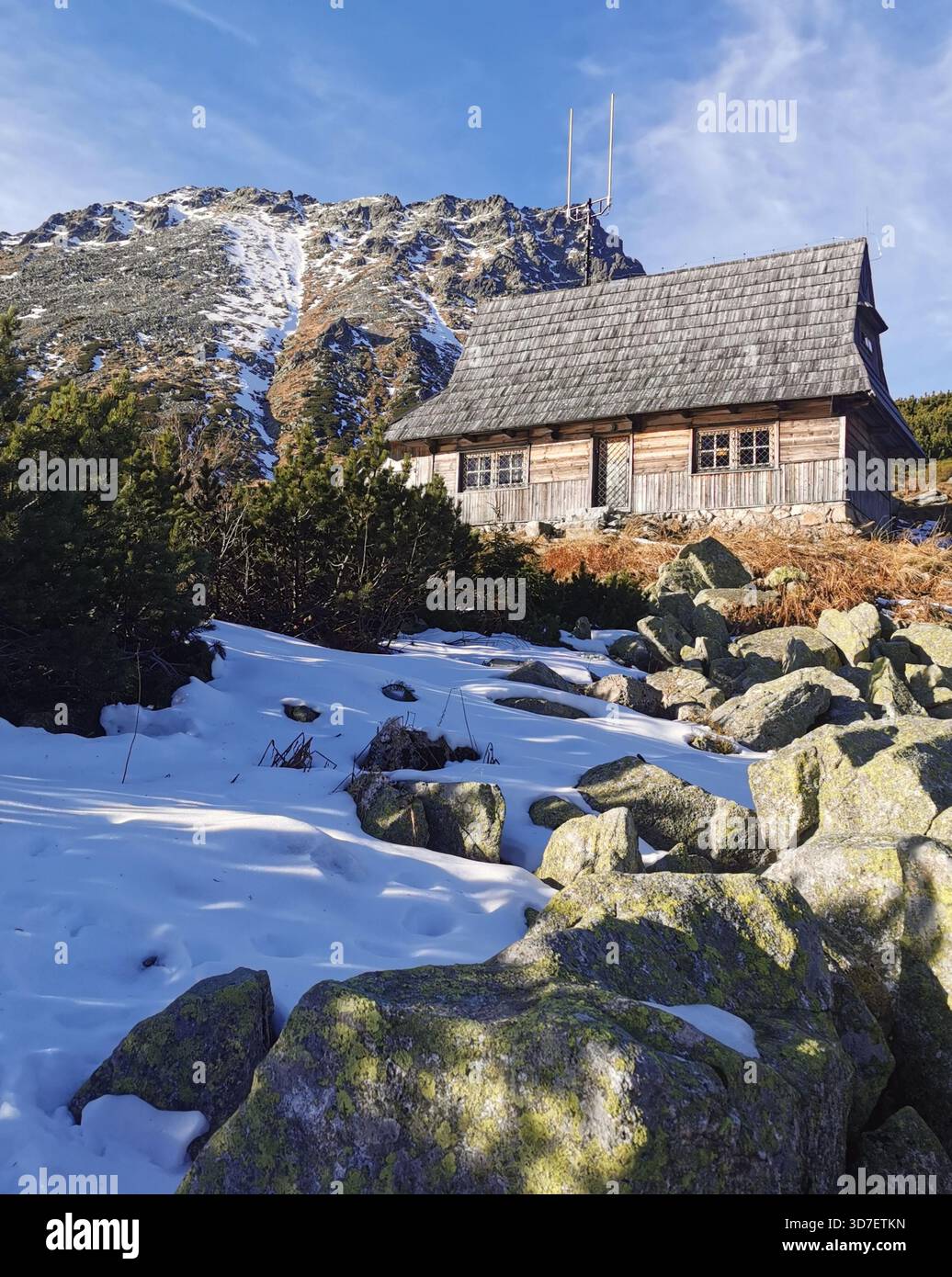 Traditional wooden hut by Mały Staw Polski in early winter, patchy snow and blue skies in the Five Polish Ponds Valley, Tatra Mountains, Poland. - Smartphone Captured Stock Image