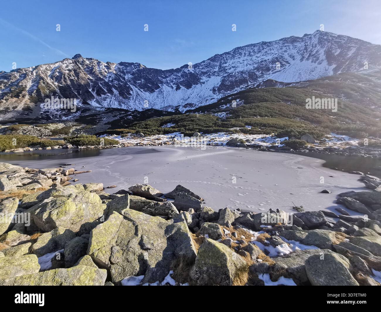 Mały Staw, Five Polish Ponds Valley (Dolina Pięciu Stawów Polskich) iced over in early winter, blue skies above an amphitheatre of snow‑brushed Tatra. - Smartphone Captured Stock Image