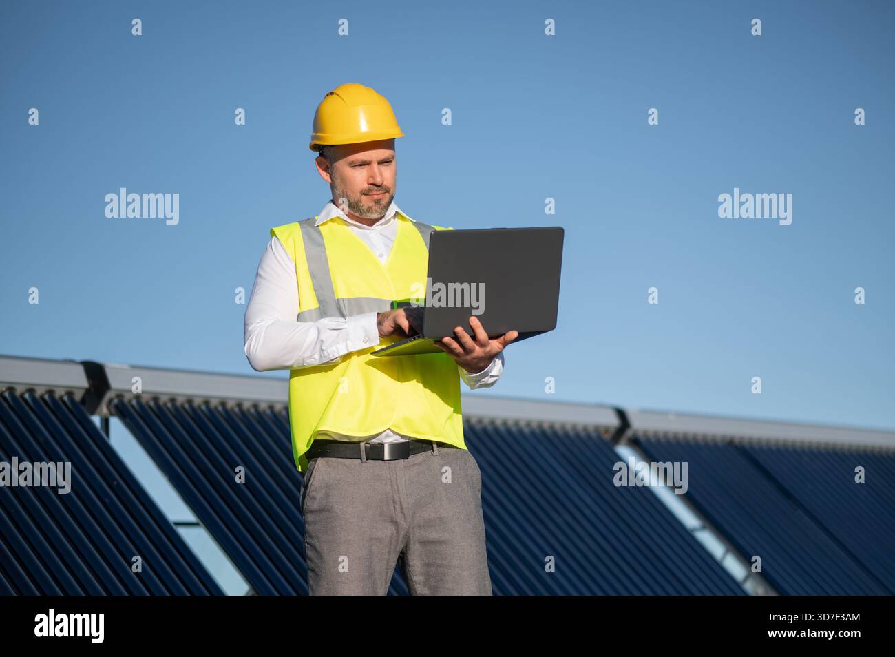 Worker with hard hat working on digital computer among solar panels Stock Photo