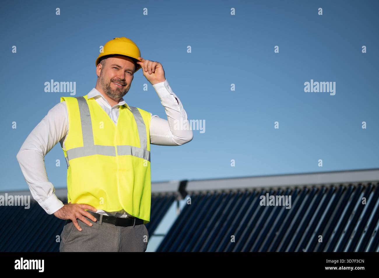 Technician in safety vest standing near solar panel field on rooftop Stock Photo