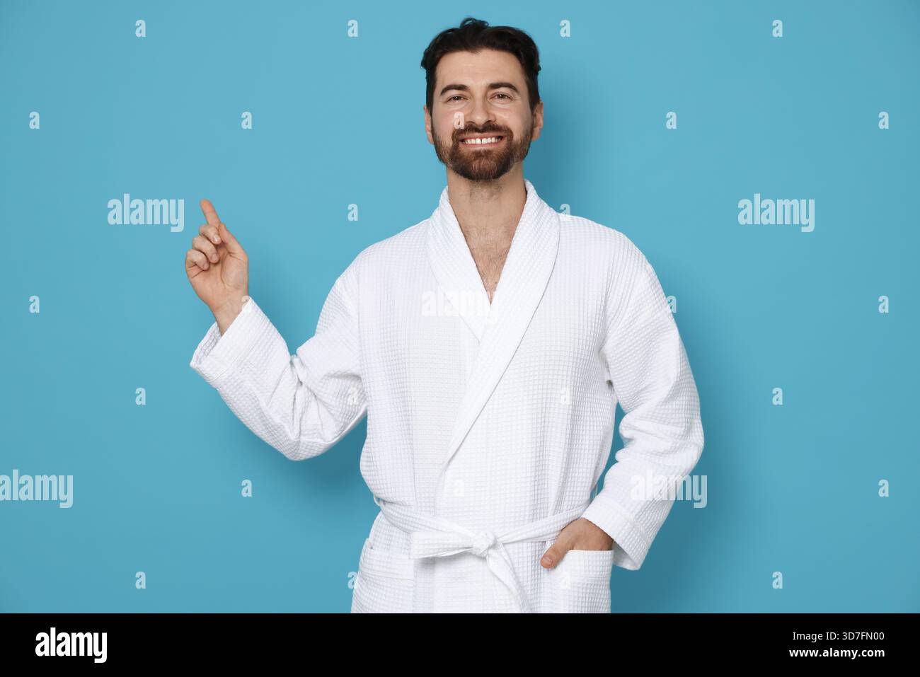 Man in bathrobe pointing at something on light blue background Stock Photo