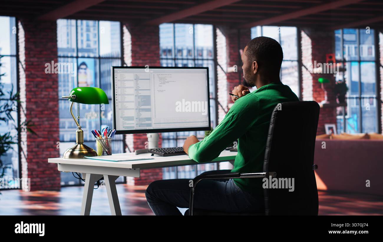 African American IT expert working with a computer full of code. Professional system engineer focuses on software development, debugging, encryption and system security at home. Camera A. Stock Photo