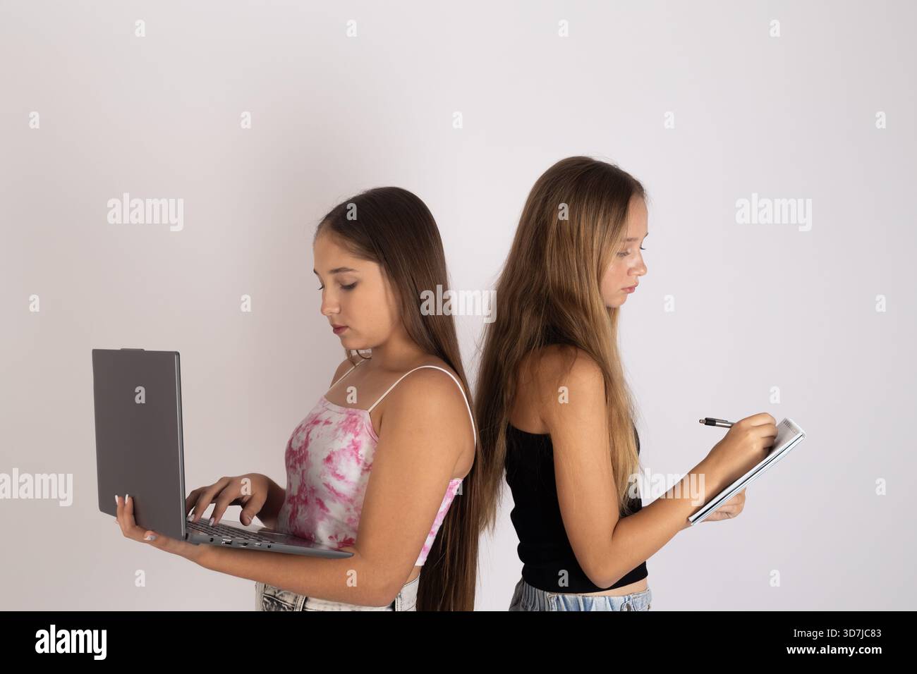girls are using electronic devices back-to-back. Stock Photo