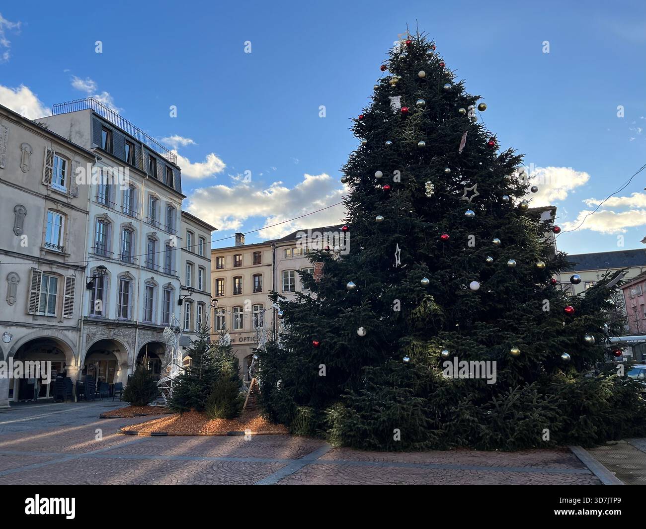 Épinal, France – 2 December 2024: A festive holiday tree illuminated with warm lights stands in the center of the square, surrounded by decorated buil - Smartphone Captured Stock Image