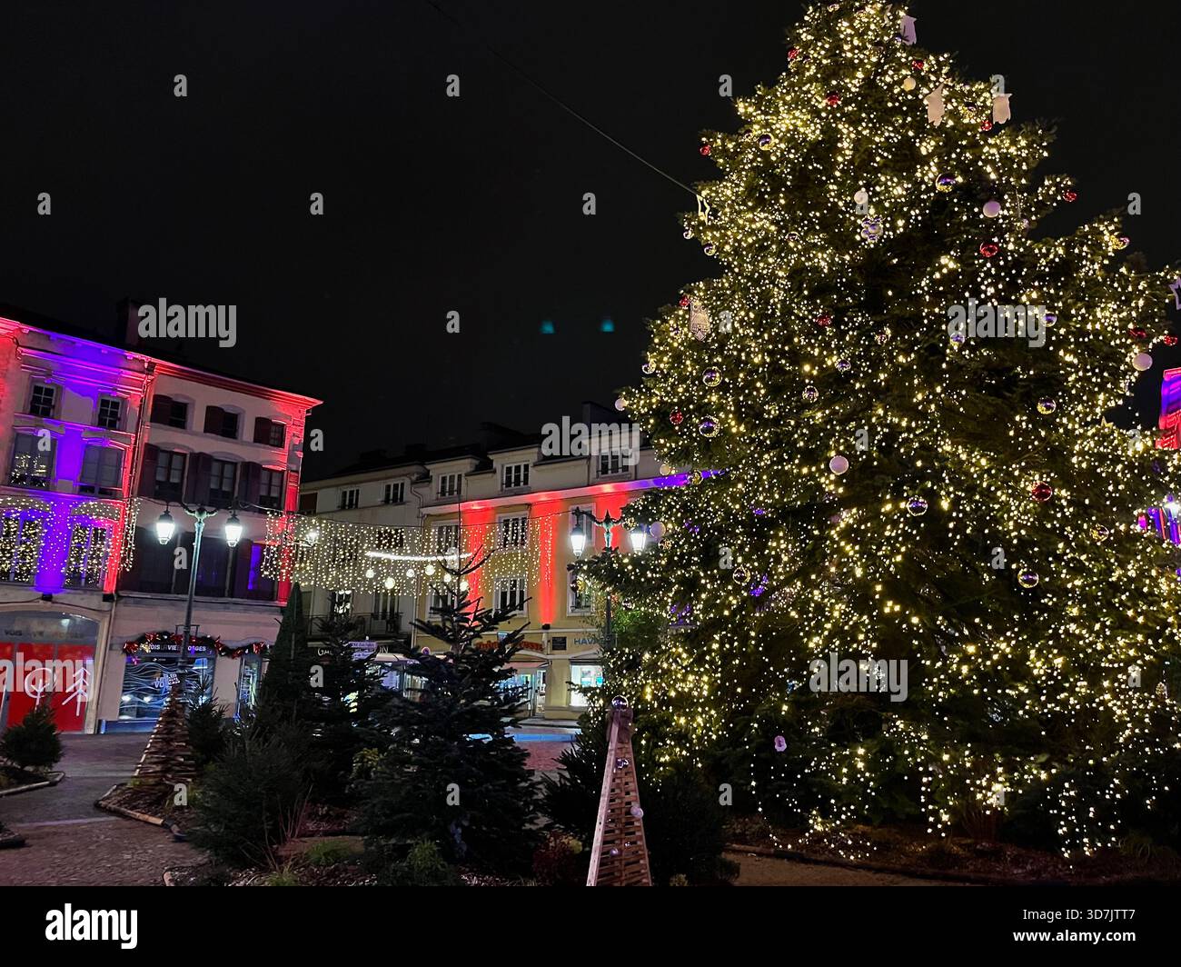 Épinal, France – December 10, 2023: Night view of a large illuminated Christmas tree on the central square, surrounded by colorful building lights - Smartphone Captured Stock Image