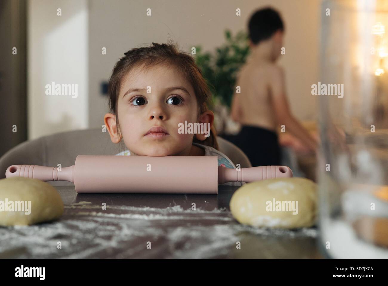 kid watches dough, child observing baking with awe, youngster pays close attention to rising bread Stock Photo