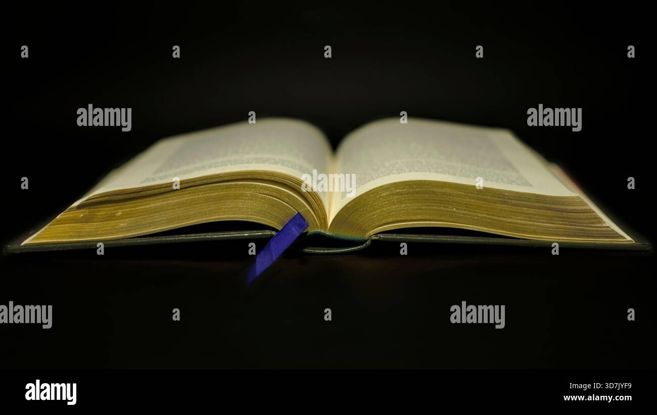 Open book with blue bookmark on black background Stock Photo