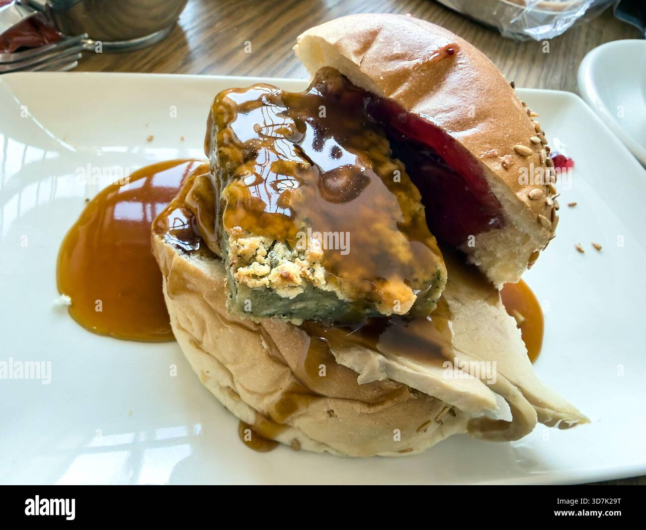 Close-up of a turkey sandwich with stuffing, cranberry sauce, and gravy on a white plate served on a wooden restaurant table - Smartphone Captured Stock Image
