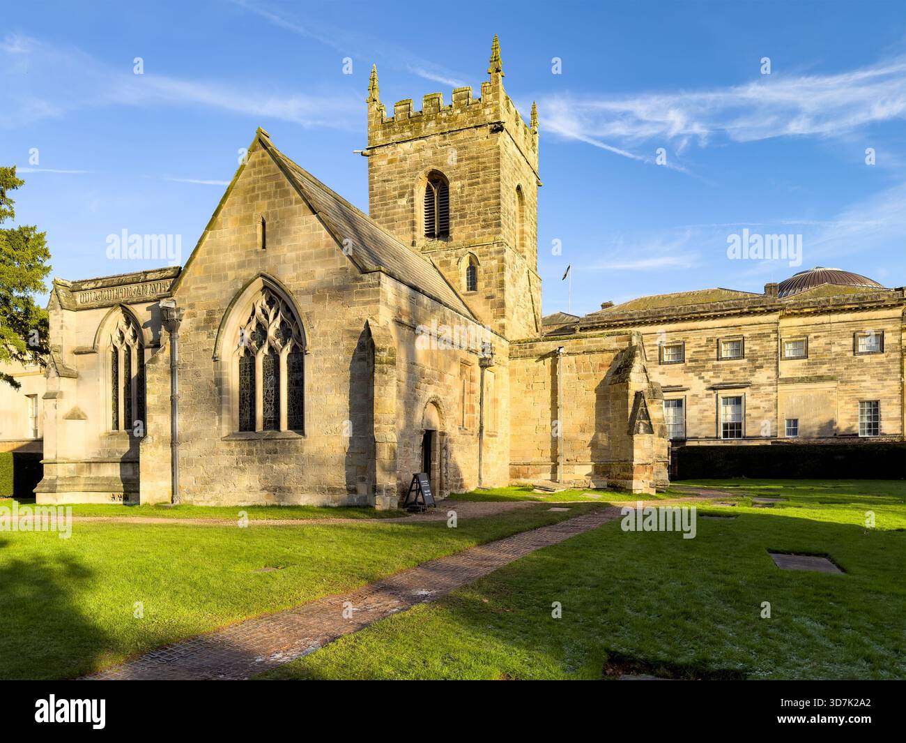 Historic stone church with arched windows and bell tower beside classical building on well-kept grassy grounds under a clear sky - Smartphone Captured Stock Image
