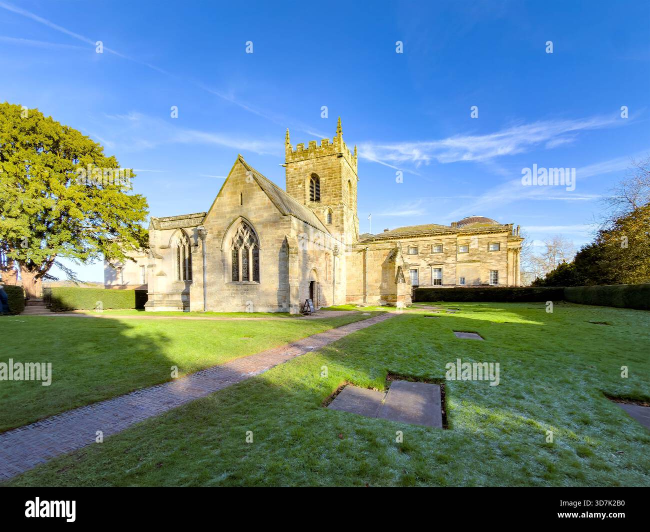 Historic stone church with arched windows and bell tower surrounded by green lawn and trees under a clear blue sky - Smartphone Captured Stock Image