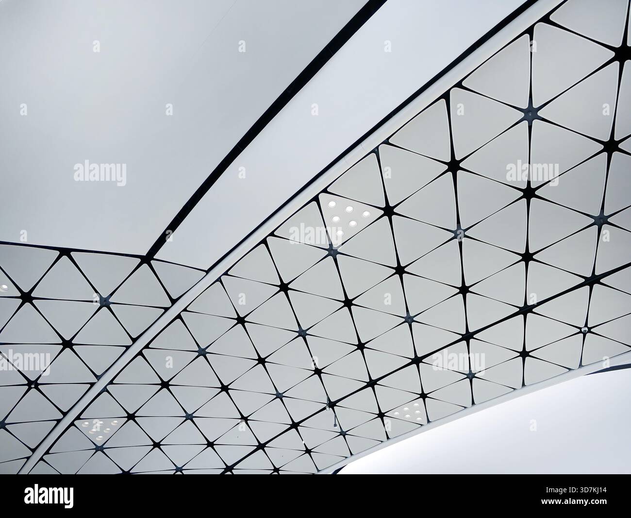 Futuristic building structure. Low angle view of a modern ceiling featuring a repeating triangular geometric pattern. Minimalist white and black grid Stock Photo