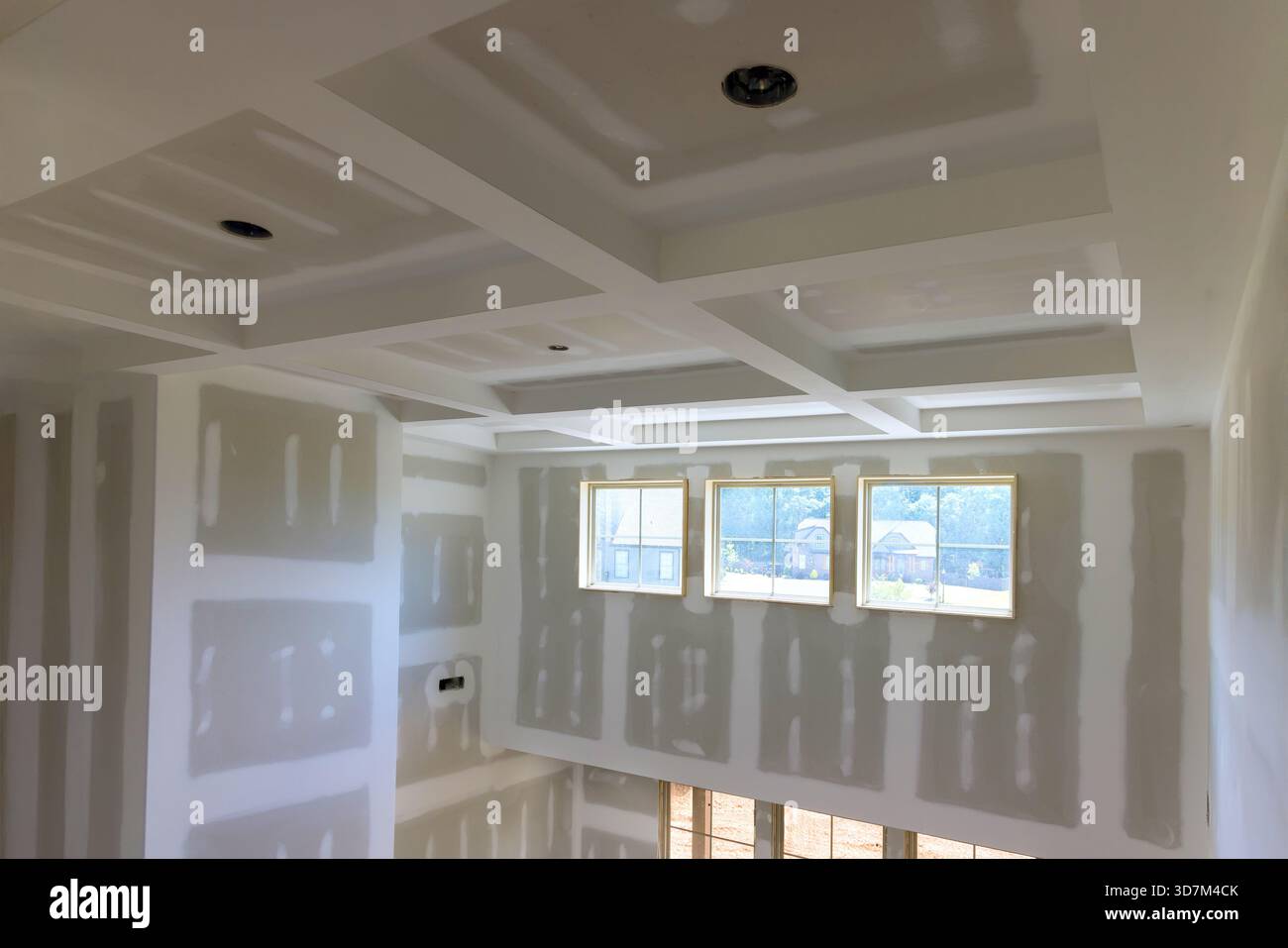 Bright living space with new drywall, coffered ceiling, ample natural light from multiple windows. Stock Photo