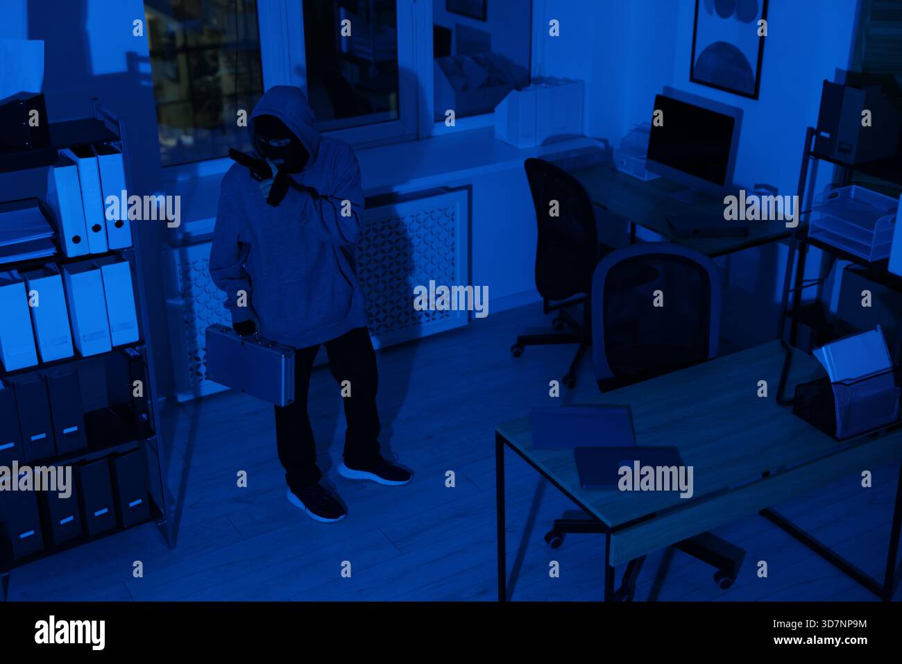 Thief with gun and briefcase in office at night Stock Photo