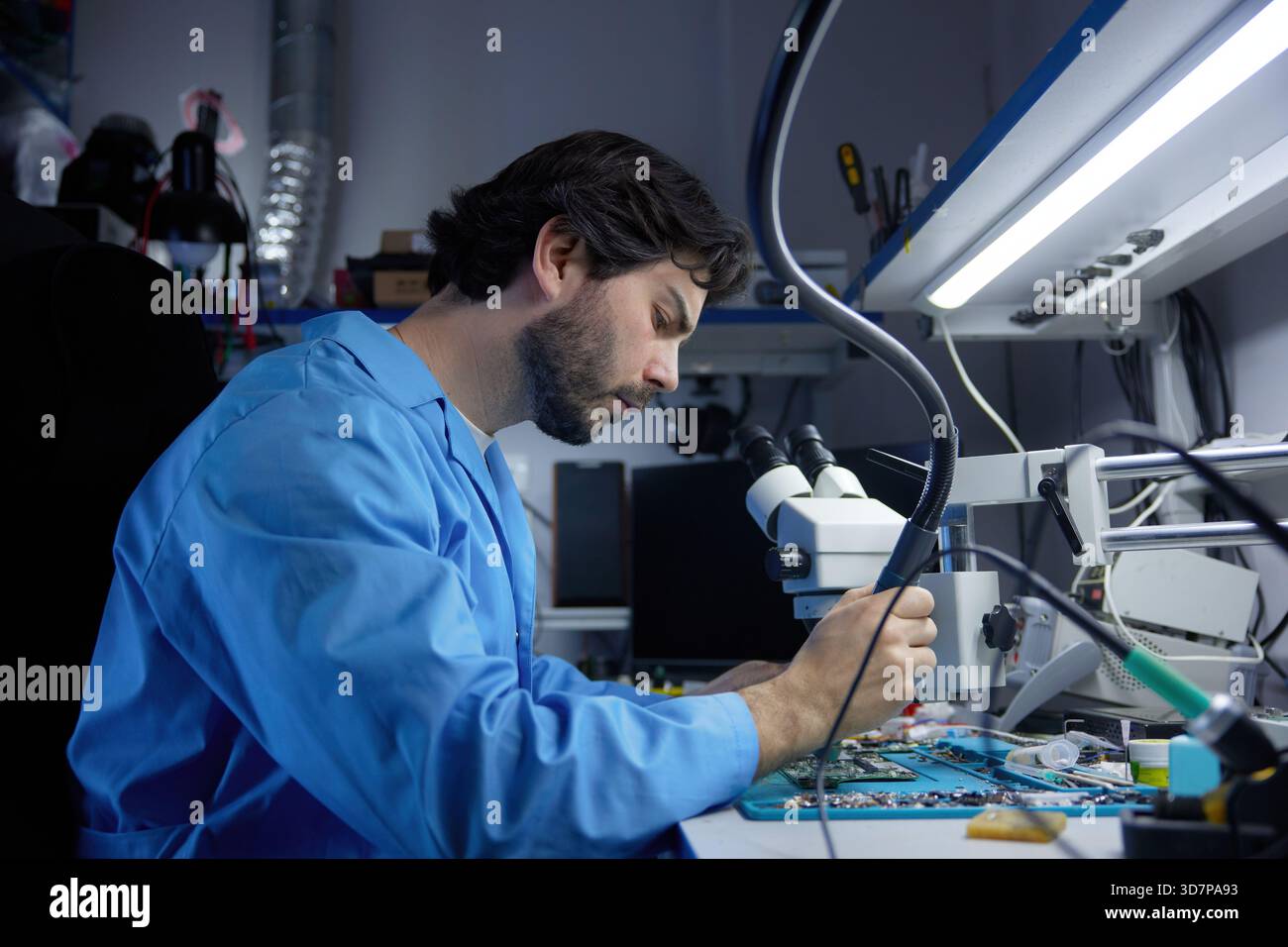A skilled technician diligently repairing laptop while working under a microscope Stock Photo