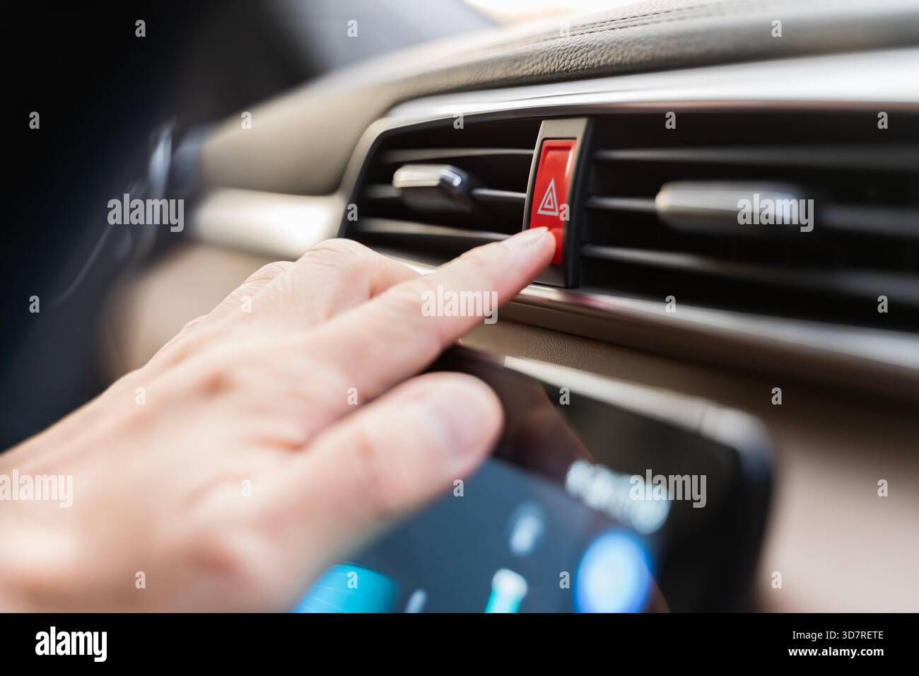 Close-up of a hand pressing the red hazard warning button on a modern car dashboard, highlighting emergency alert control, safety awareness, and vehic Stock Photo