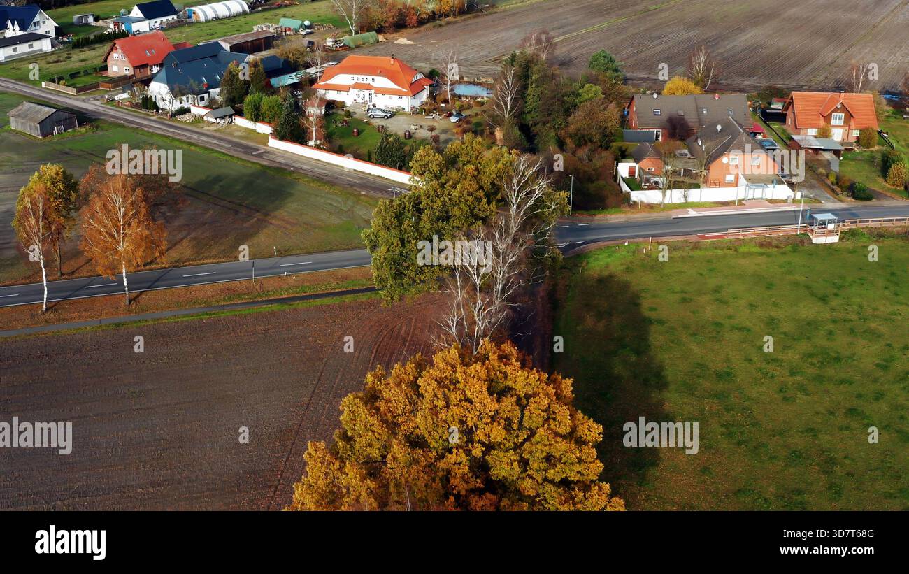 Aerial perspective captures a countryside village, featuring rural homes, farmland, a meandering road, and vibrant autumn foliage Stock Photo