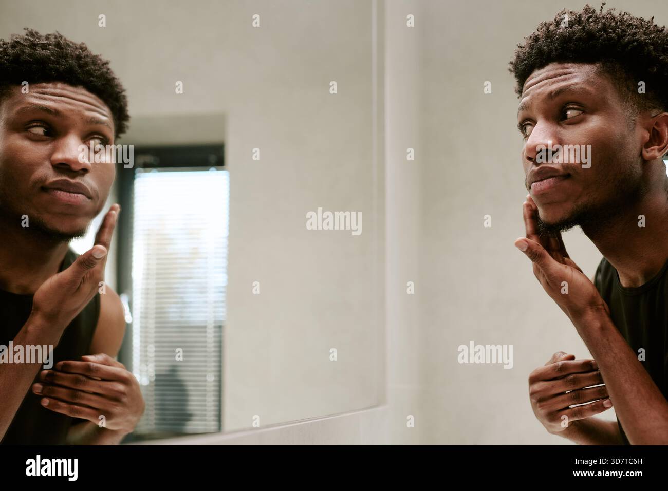 Young Adult Black Man Touching Face While Looking at Reflection in Mirror Stock Photo