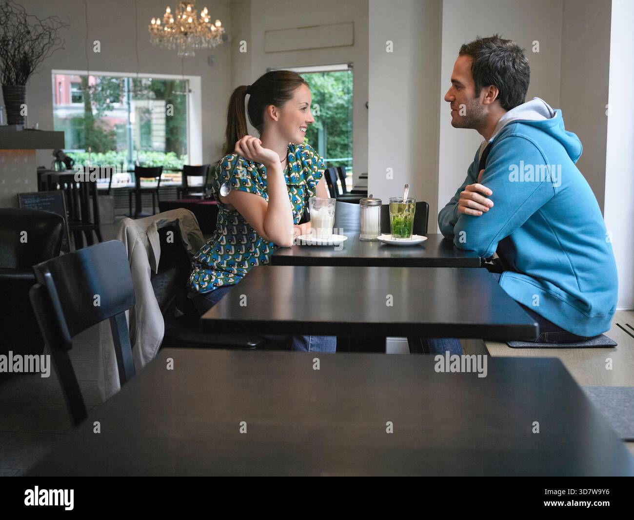 A couple enjoys a conversation over drinks in a cozy, modern cafe interior. Germany Stock Photo